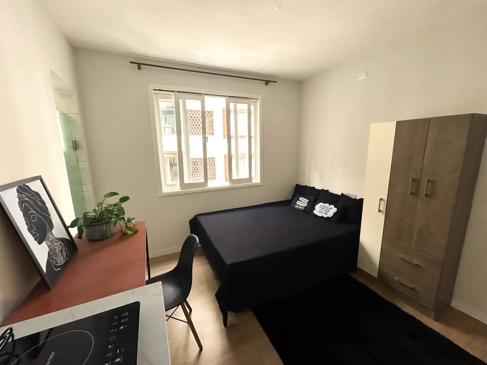 Estúdio com cama de casal junto à janela e armário de três portas