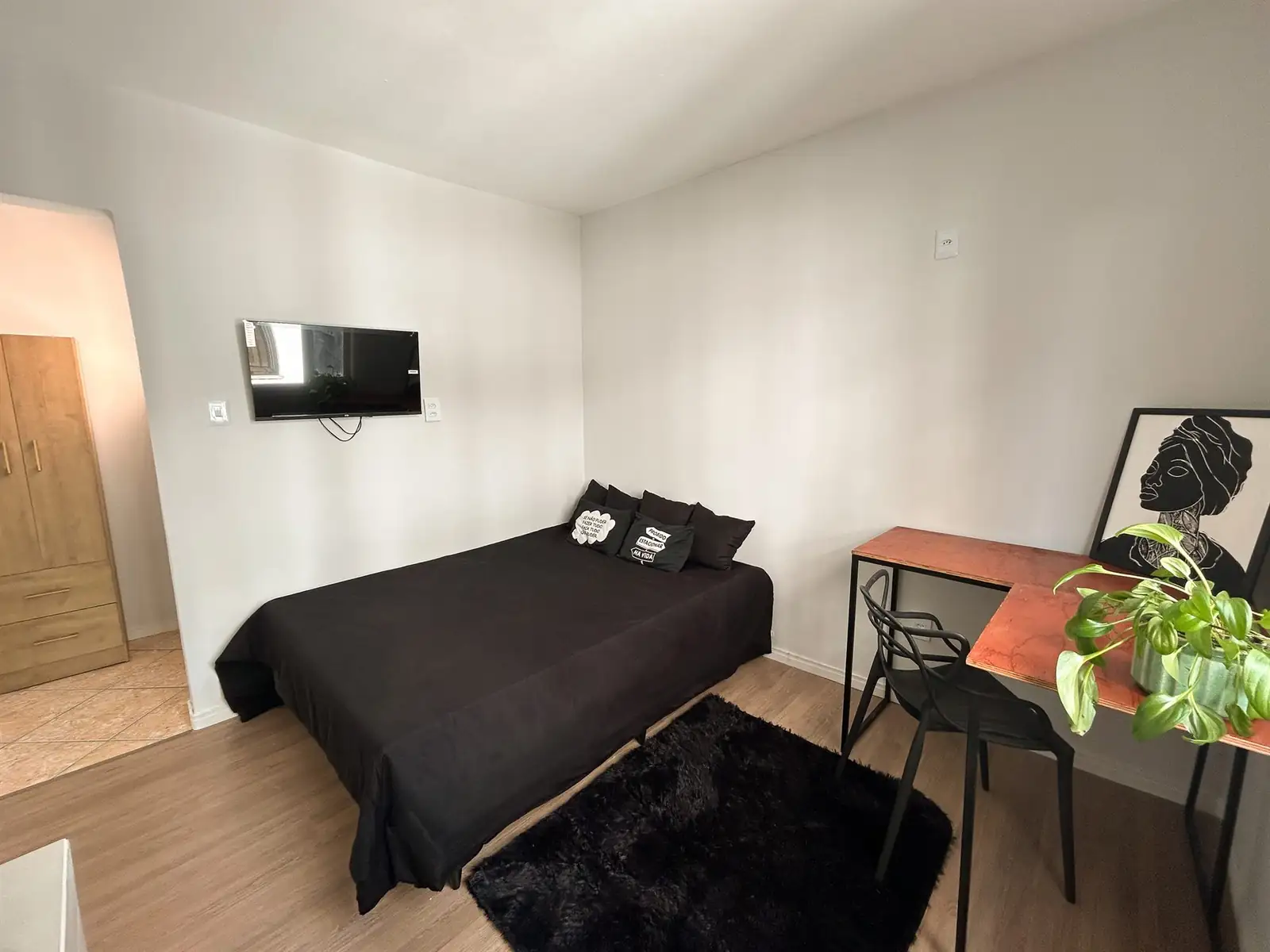Cama de casal do estúdio com TV na parede e armário ao lado